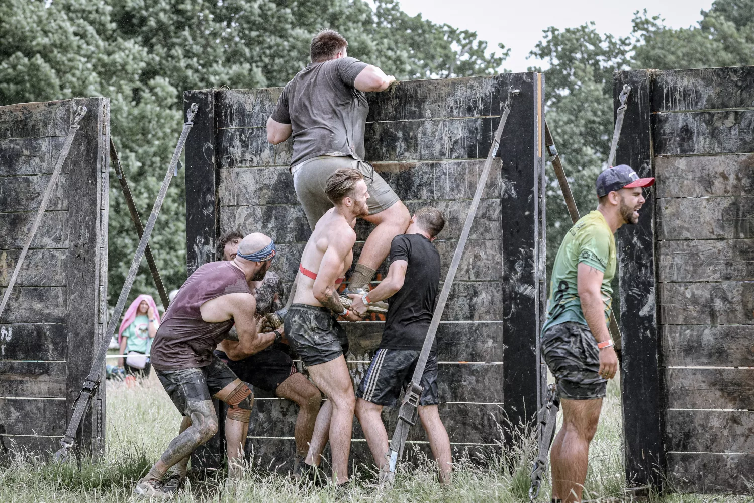 A group of people helping each other over a high wall covered in mud