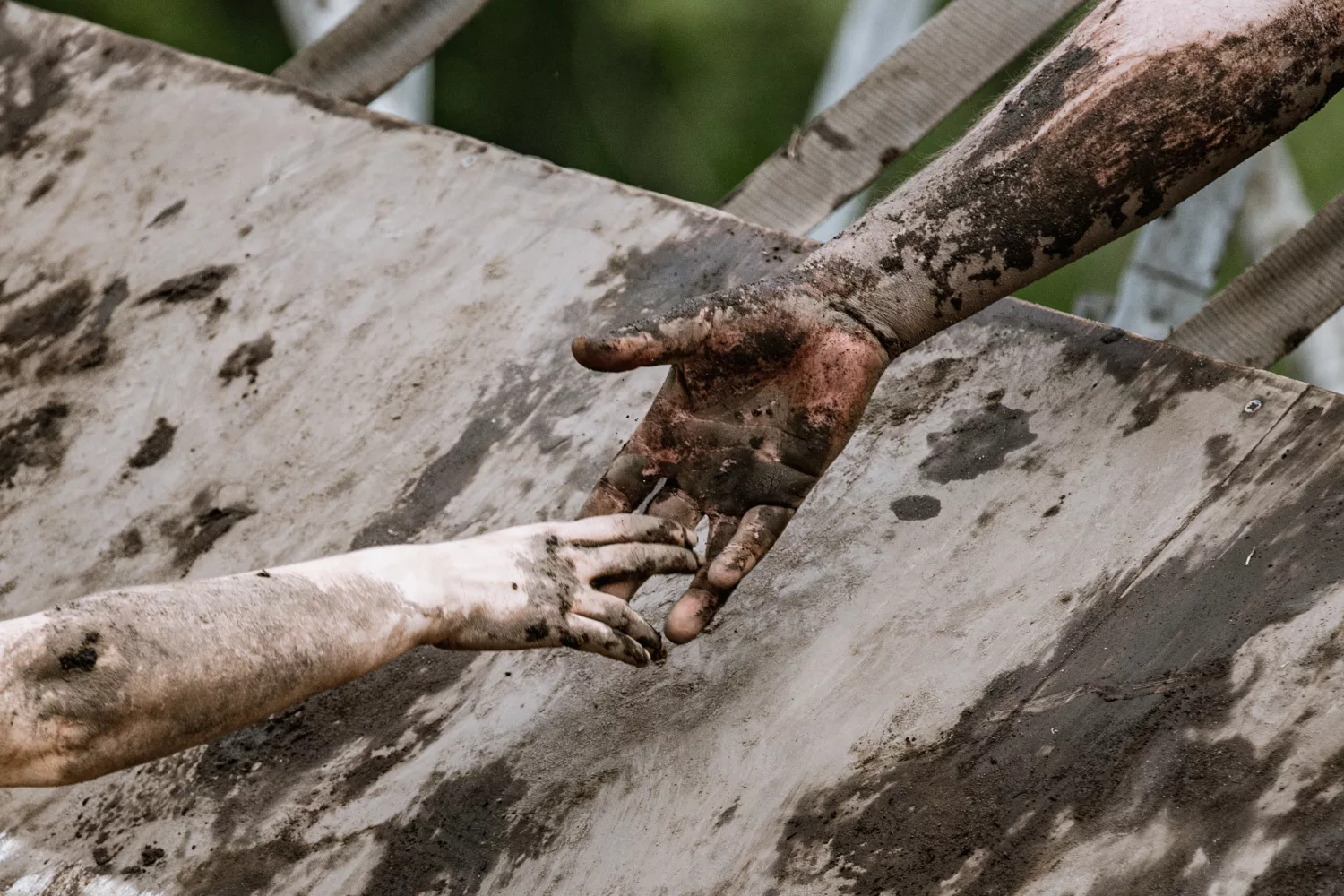 Muddy hands reaching towards each other to pull up an obstacle