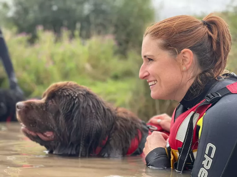 A woman swimming in a lake with a Newfoundland dog